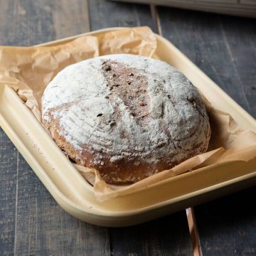 Rundes, gebackenes Brot mit bemehlter Kruste auf einer Brotbackplatte mit Backpapier.