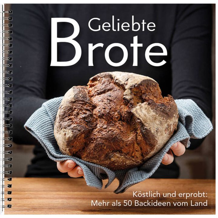 Eine Person hält ein rundes, gebackenes Brot in einem Handtuch. Auf dem Cover steht "Geliebte Brote", darunter "Köstlich und erprobt: Mehr als 50 Backideen vom Land". Spiralbindung erkennbar.